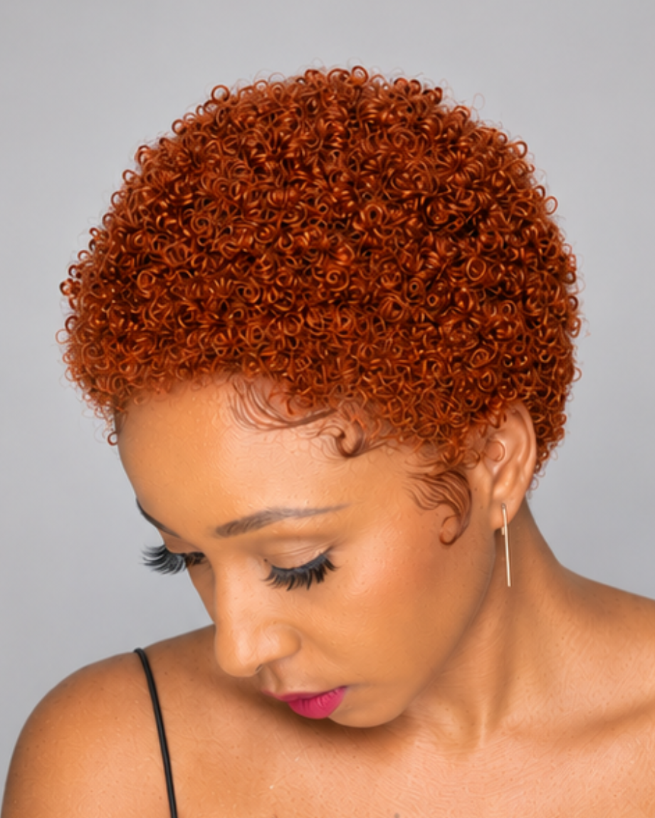 A woman with a short, tightly curled, low-ploofing crooked wig in a vibrant coppery orange-red color, shown from the chest up against a solid gray background.
