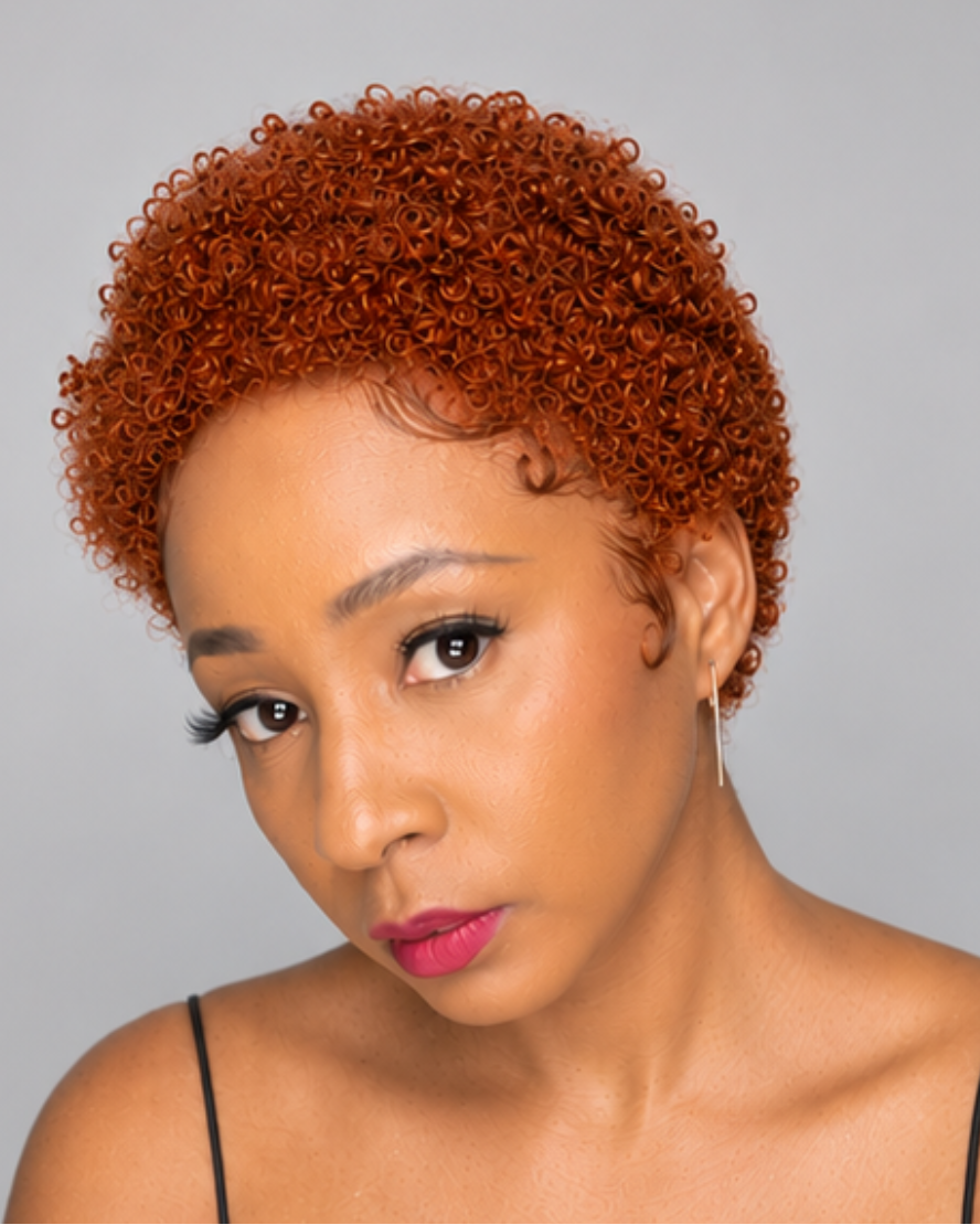 A woman with a short, tightly curled wig in a warm coppery orange-brown shade, looking down against a solid gray background.