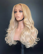 22-inch Vietnamese glueless wig in ash blonde with layered bouncy waves  on a mannequin head with shoulders on a tripod against a gray studio background
