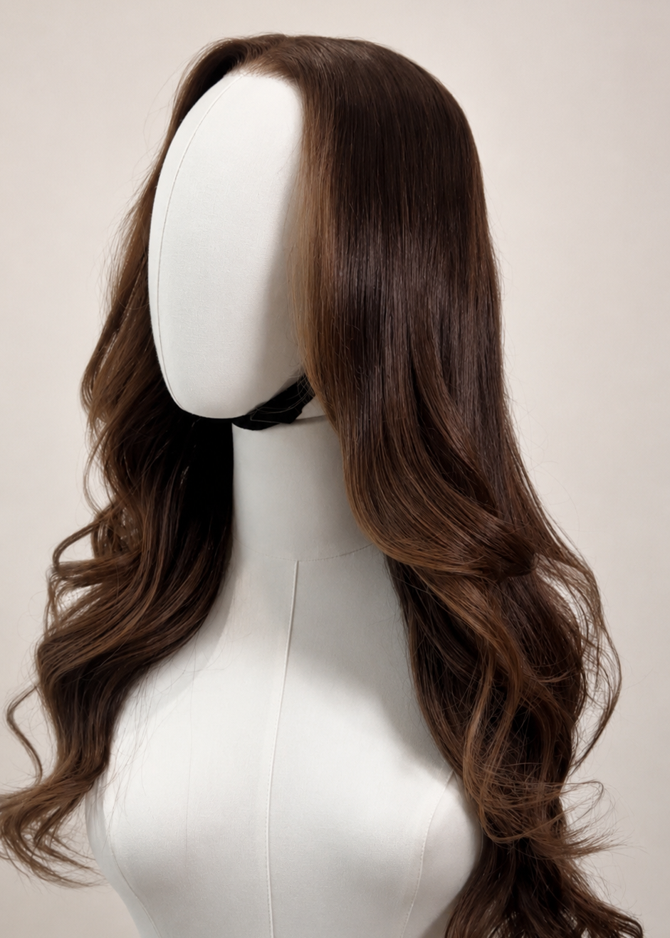 A long, wavy brown wig with side-swept bangs displayed on a white mannequin head against a light beige background.