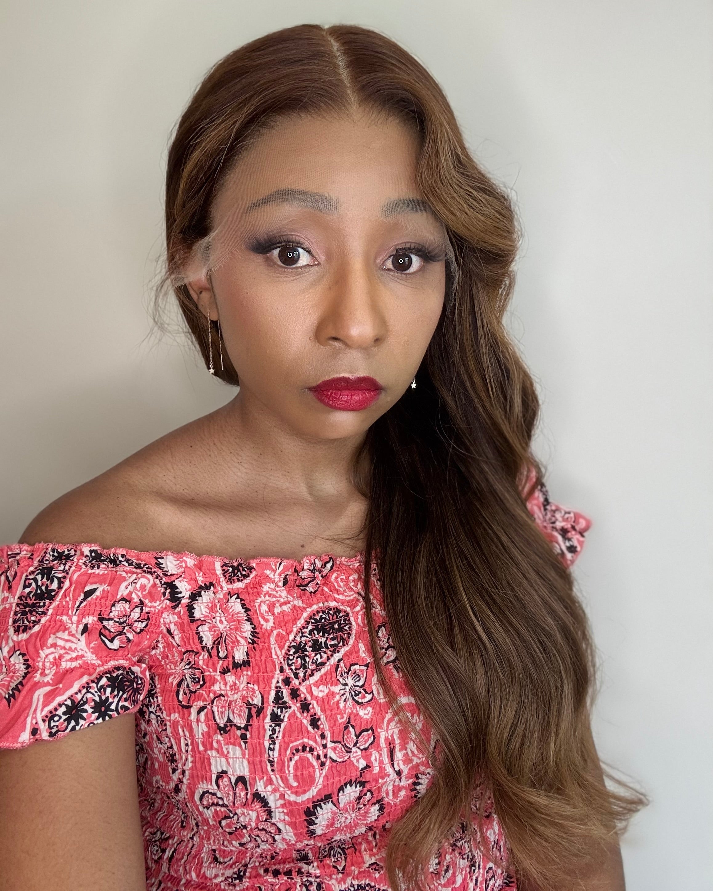 Woman with long brown hair wearing a pink and black patterned top against a plain background