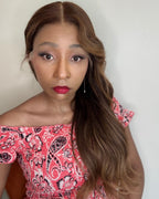 Woman with long braided hair wearing a pink patterned dress against a plain background