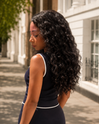 Woman in a black dress standing on a sunlit street with trees and buildings in the background