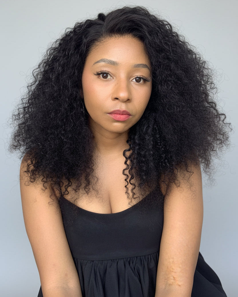 A woman with voluminous, curly black hair wearing a black sleeveless top, photographed against a solid light gray background.