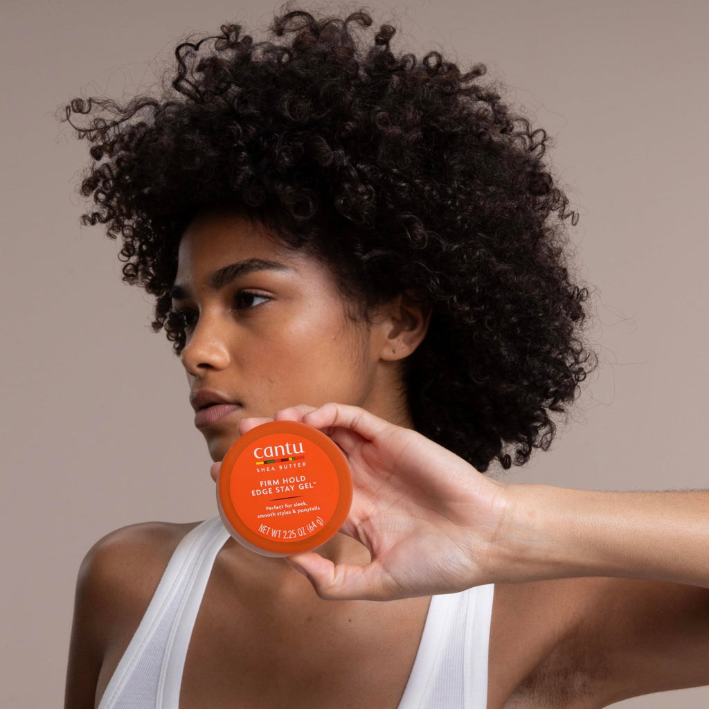 Woman holding an orange can of Cantu hair product against a neutral background