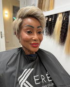 Woman in a hair salon wearing a Kerê hair cape with hair extensions displayed in the background.