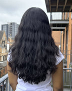 Person with long wave Indian raw hair standing on a balcony with buildings in the background