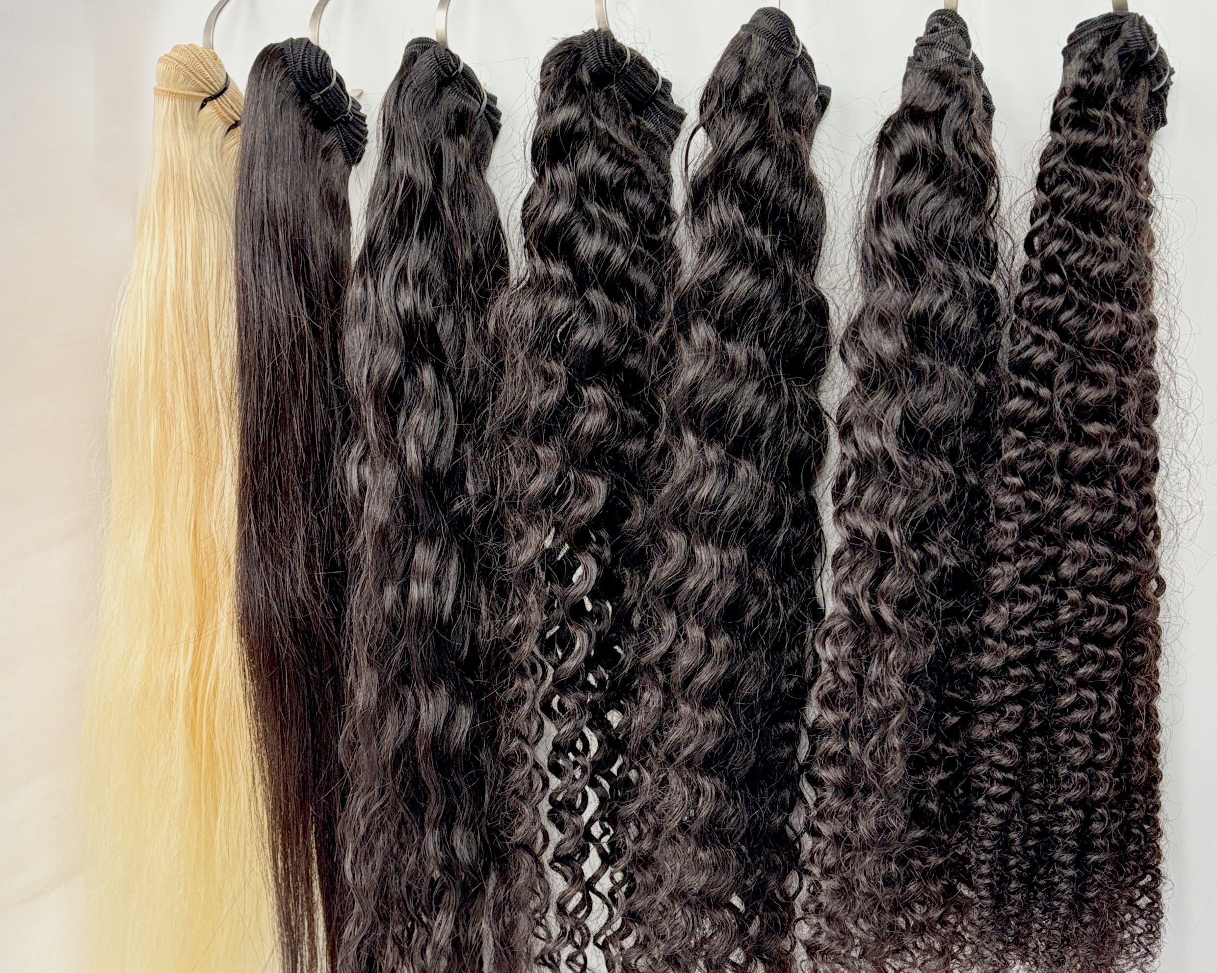 Collection of raw hair extensions ranging from straight to tight curl pattern on a white background