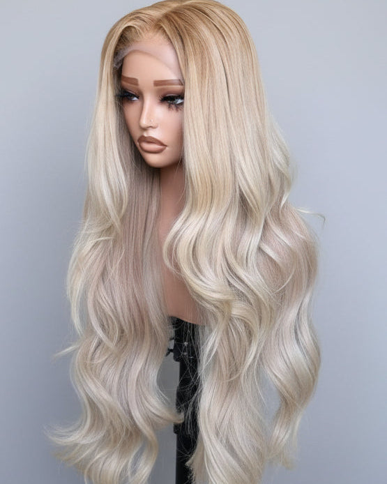 26-inch Vietnamese glueless raw hair wig in ash blonde with layered bouncy waves  on a mannequin head with shoulders on a tripod against a pastel olive green wall.